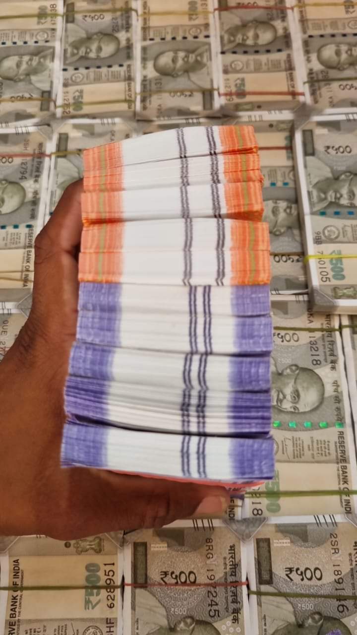Hand holding orange and purple Indian banknotes over a background of 500 rupee notes.