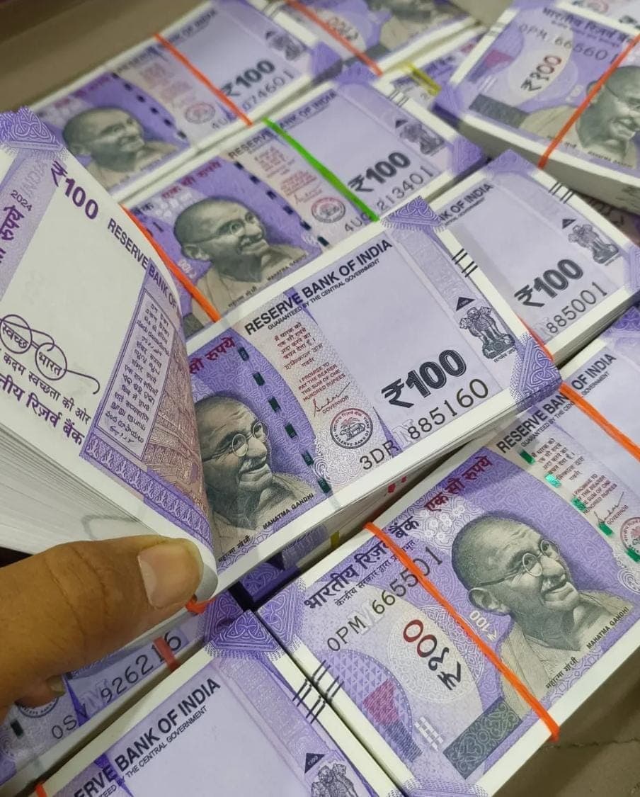 Hand flipping through a stack of purple Indian 100 rupee notes featuring Mahatma Gandhi.