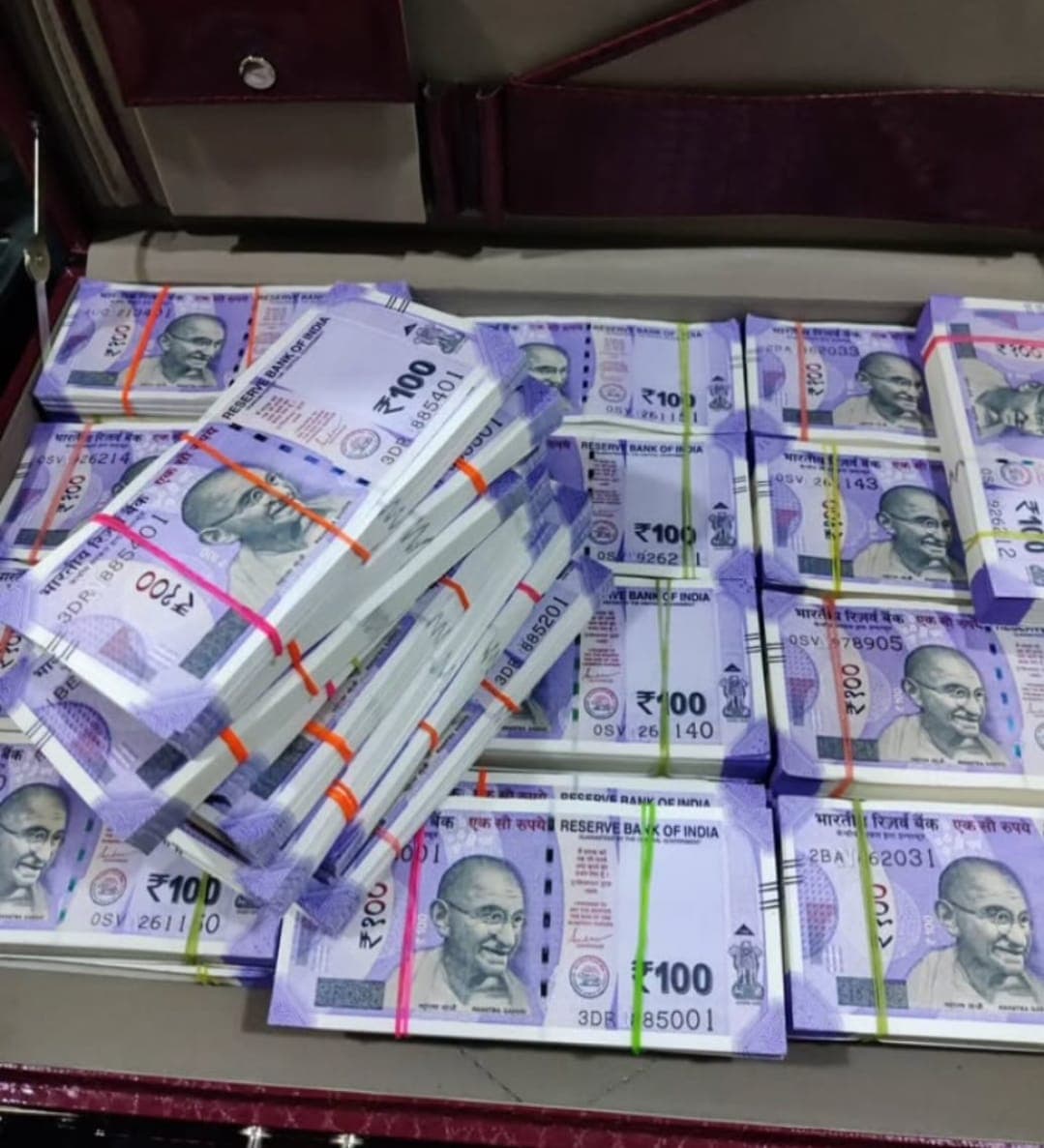 Stacks of purple Indian 100 rupee banknotes featuring Mahatma Gandhi inside an open briefcase.